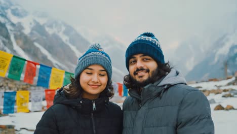 young tourists wearing winter clothes smiling and enjoying snowy mountain landscape with colorful buddhist prayer flags, celebrating their holidays in a peaceful environment