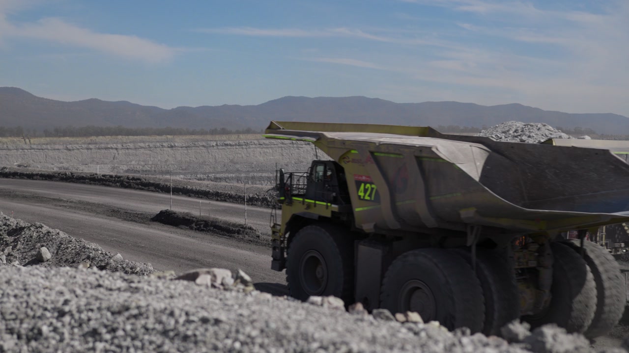 Massive mining haul truck carrying overburden along haul road in open-cut coal mine. Industrial resource extraction, heavy machinery, and large-scale earthworks in remote landscape.