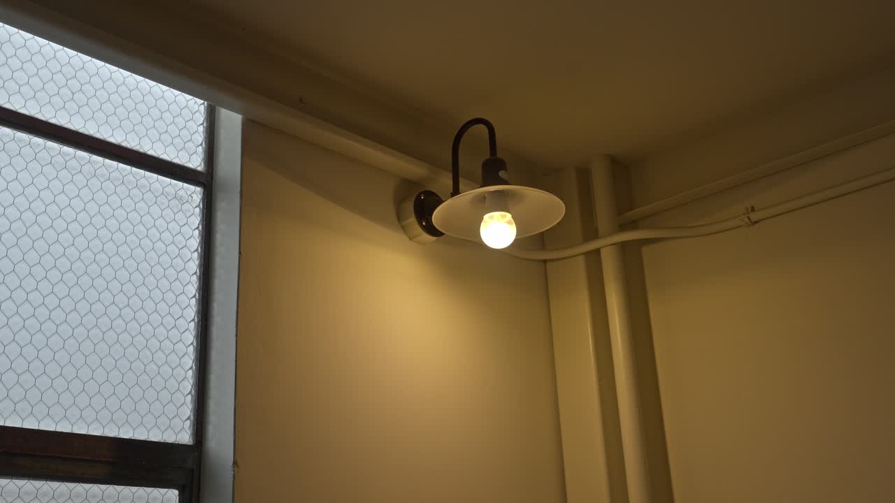 A simple wall light illuminates the interior of a retro building, with a textured glass window creating a soft, diffused glow.