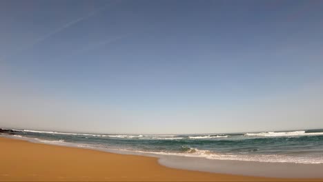 Guincho:-Amidst-the-tropical-beauty,-a-young-surfer-donning-a-wetsuit-stands-alone-on-the-sandy-shore,-gazing-at-the-sea-under-the-sunny-sky