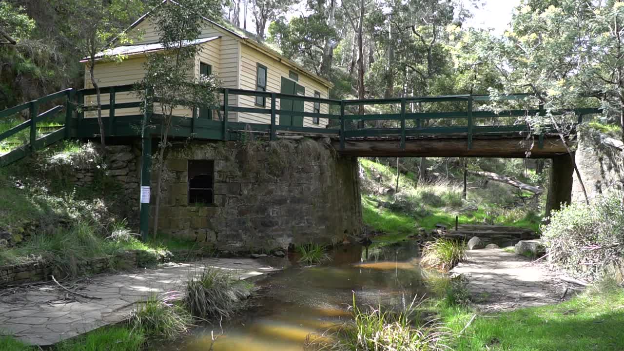 fotografía de un viejo puente de madera y piedra sobre un arroyo o arroyo, junto a un cobertizo de tablas de intemperie en el monte australiano