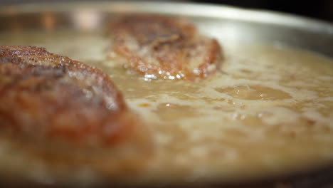 golden brown chicken breasts simmering in a savory sauce - close up slow motion