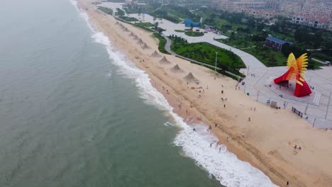 aerial view flying from the sea toward sandy beach, bright red and yellow monument and sand sculptures
