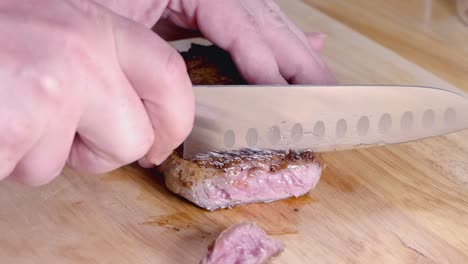 Slow-Motion-Shot-of-Slicing-a-Medium-Rare-Ribeye-Steak-on-a-Wooden-Cutting-Board