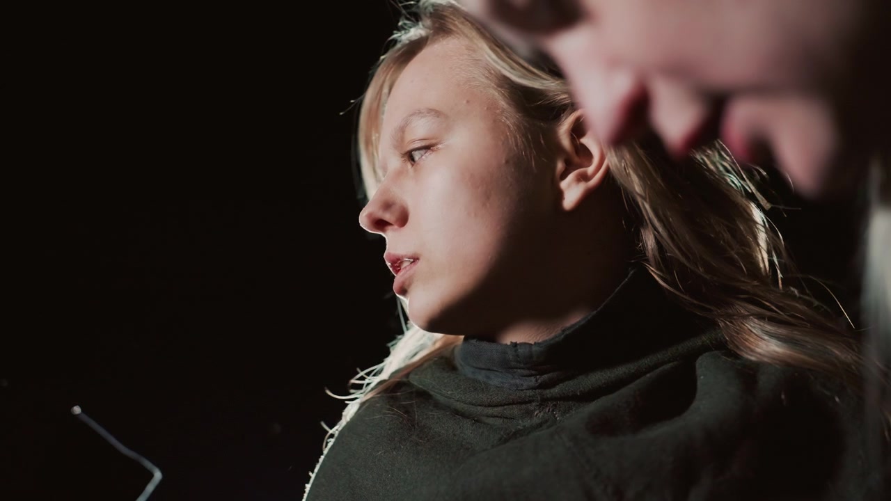 Primo piano di profilo di una giovane donna che gira la testa a sinistra con i capelli all'indietro e una forte retroilluminazione che crea un controluce lungo i capelli e la spalla, mentre un'espressione tesa e concentrata suggerisce un improvviso dramma.