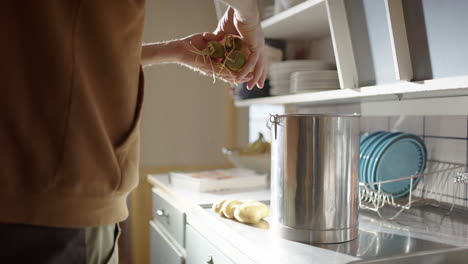 manos caucásicas que arrojan verduras obsoletas en un contenedor de compost de metal