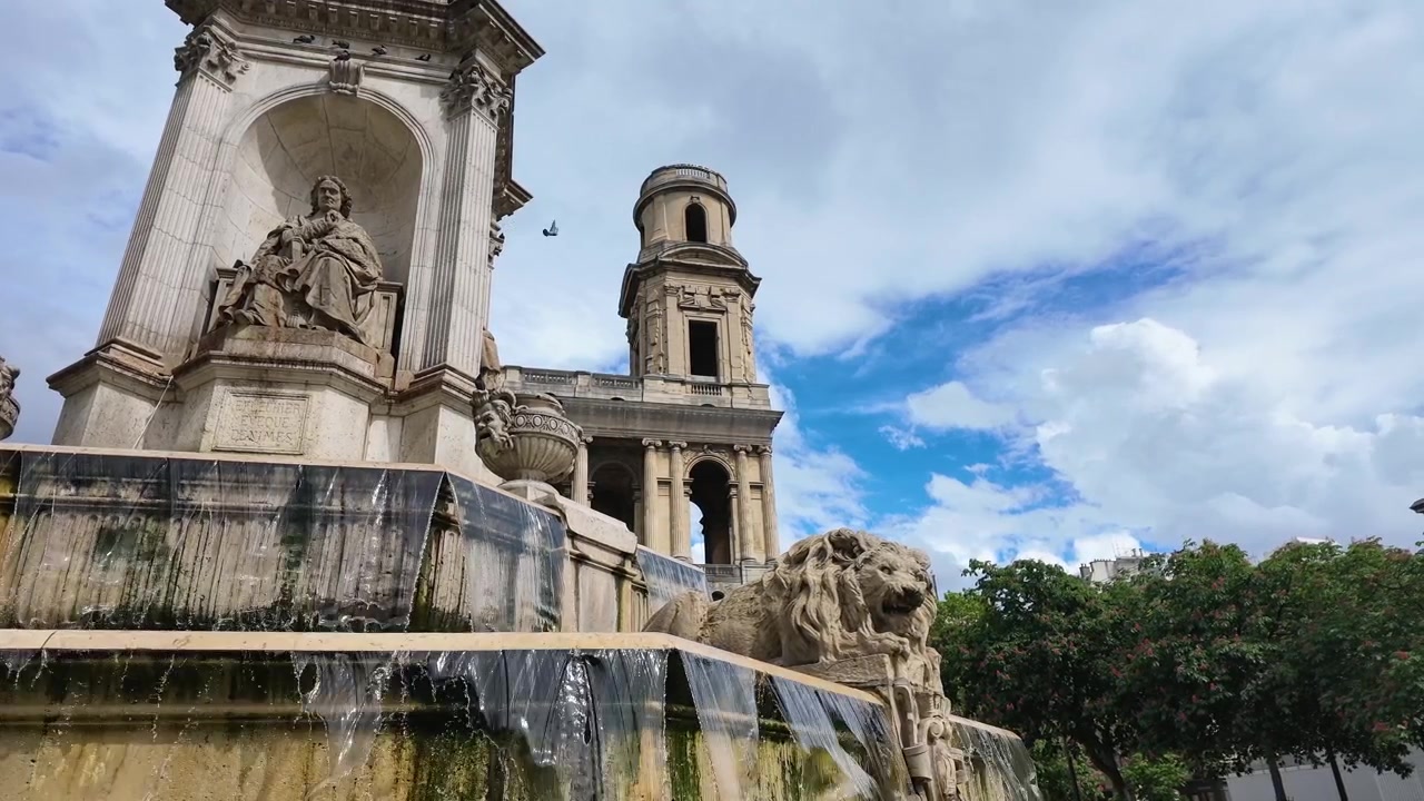 Inquadratura dal basso di acqua che scorre alla fontana di Saint Sulpice con il campanile della chiesa sullo sfondo.