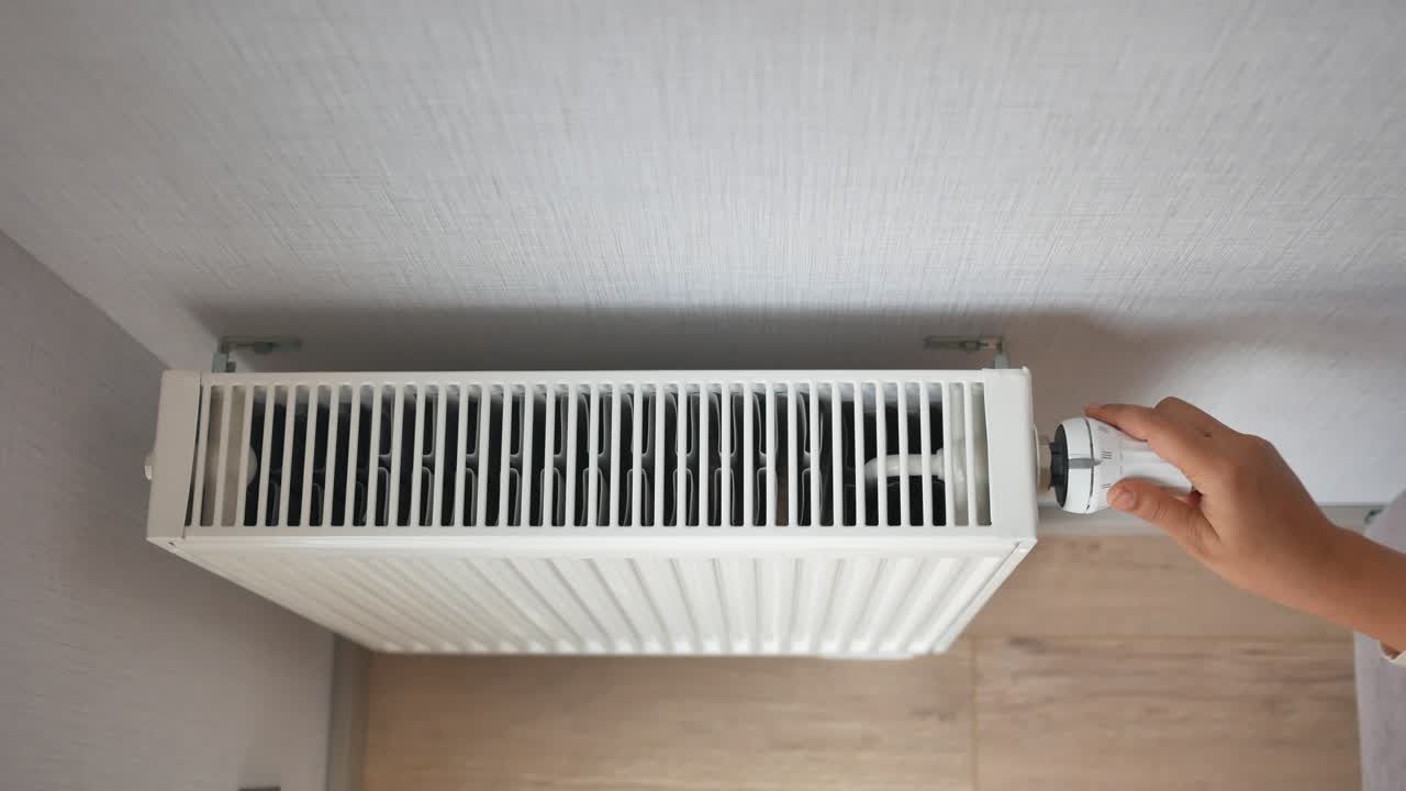 벽에 장착 된 라디에이터 온도 조절기를 조정하는 사람