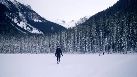 woman walks through snow toward scenic winter forest mountains, canada