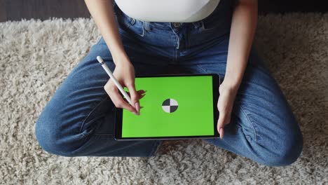 mujer se sienta en posición de loto y dibuja con el lápiz en una tableta electrónica con pantalla verde, vista superior. maqueta. concepto de arte de creatividad digital