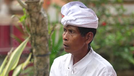 balinese man dressed in traditional clothing for temple ceremony smoking a cigarette outside