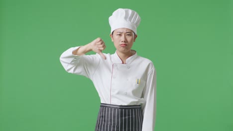 asian woman chef showing thumbs down gesture to camera while standing in the green screen background studio