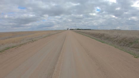 point of view driving on a straight stretch of gravel road and past a farm yard with grain bins and barn