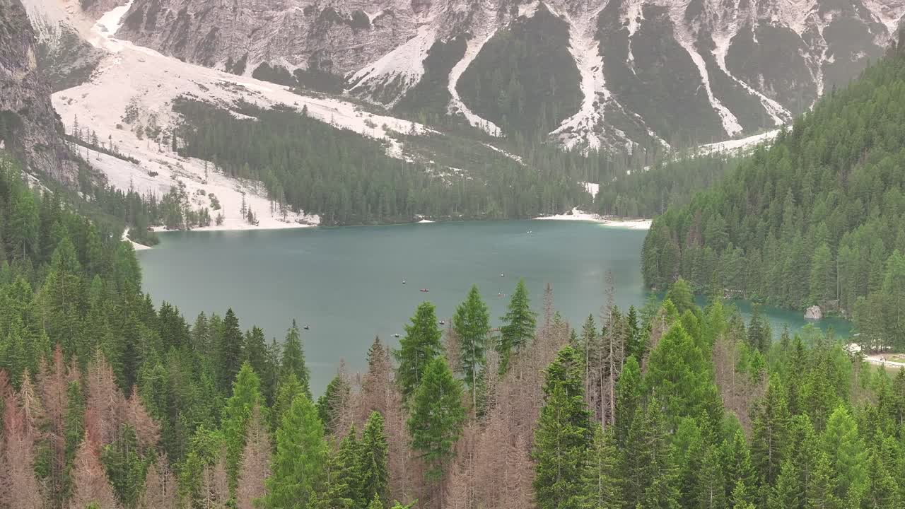 Lake Braies surrounded by dense pine trees and mountains under an overcast sky with snow patches