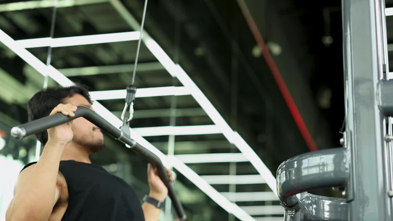 A man exercises on a lat pulldown machine in a well-lit gym, showcasing strength and focus