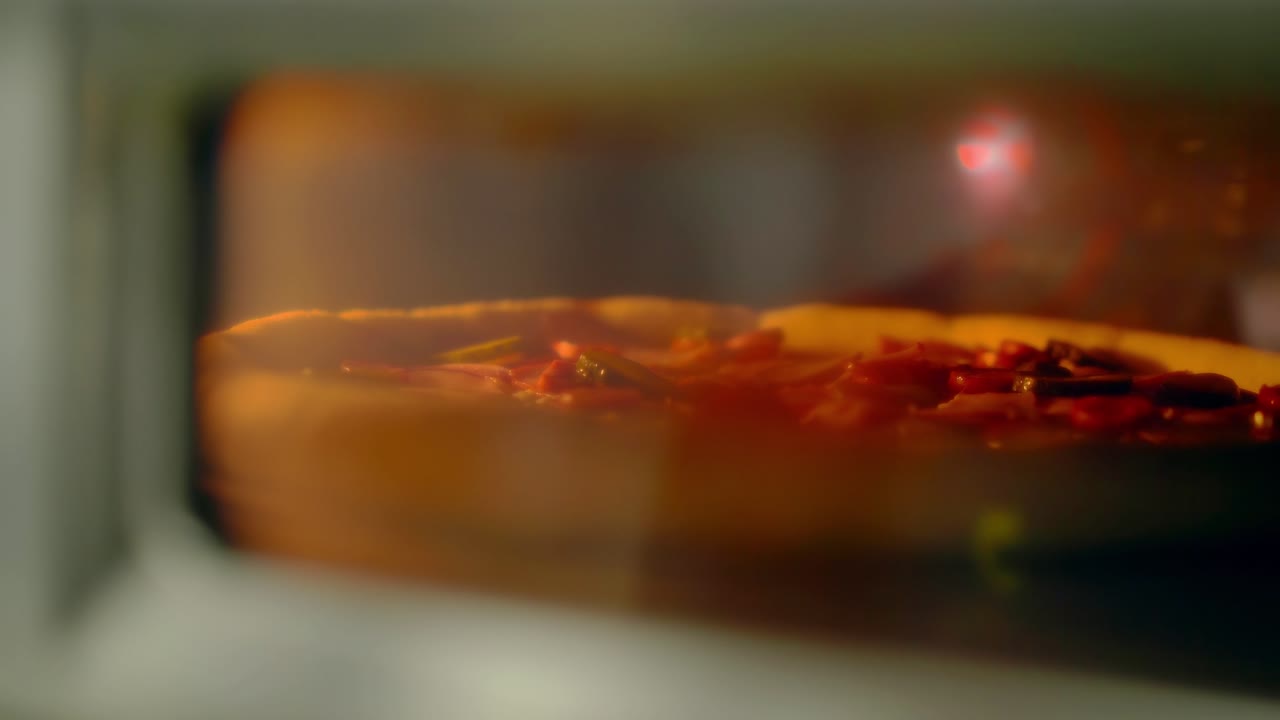 pizza con tocino y verduras está horneada en el horno vista a través de la ventana