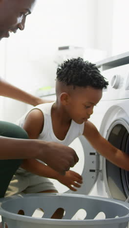 side view of black father and son washing clothes in washing machine at comfortable home 4k