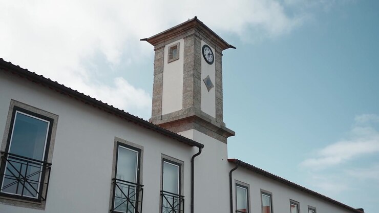 Classico edificio bianco con finestre e balconi dalla struttura nera, sormontato da una storica torre dell'orologio in pietra sotto un cielo azzurro terso