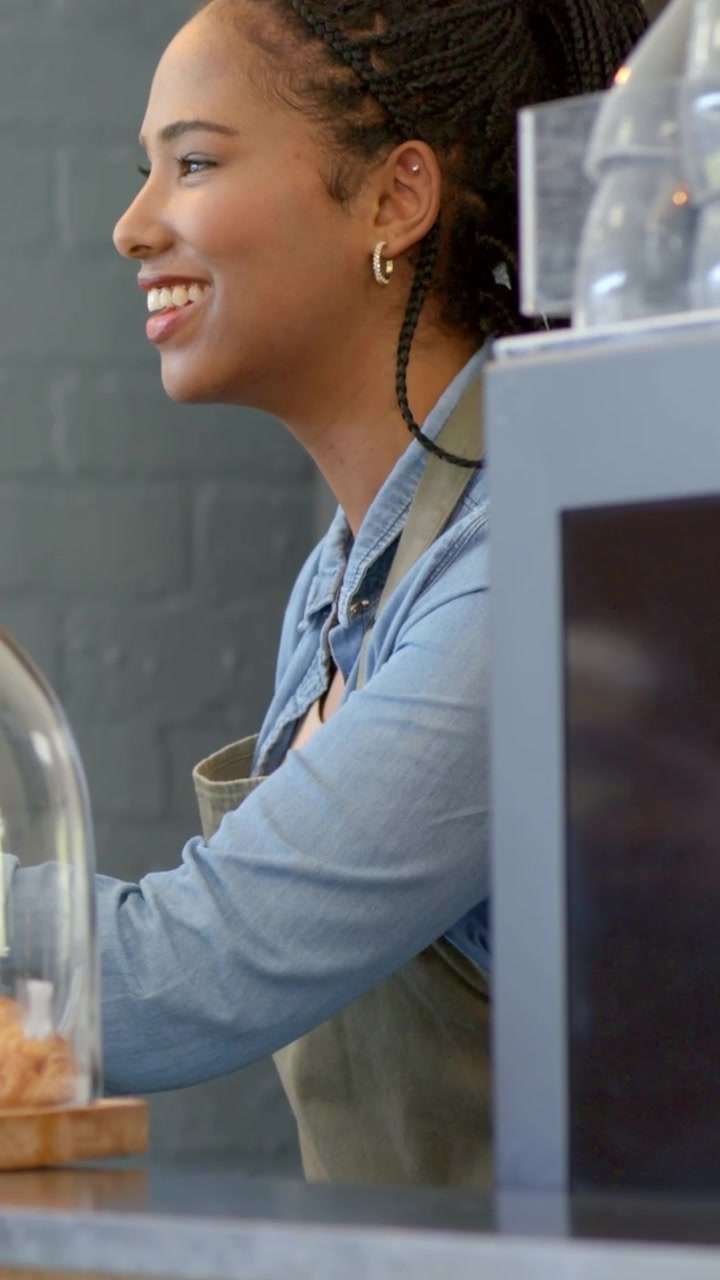 Vertical video: Responding customer ordering, barista in apron reaching for cloche at cafe counter
