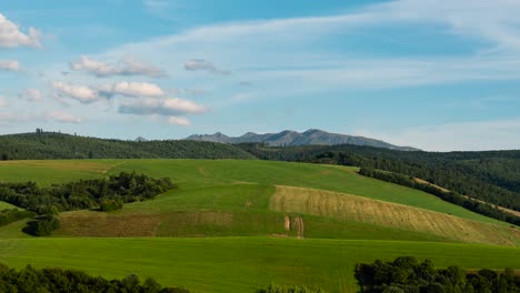 timelapse over rolling hills and mountains in distance with moving clouds, daytime to sunset push in