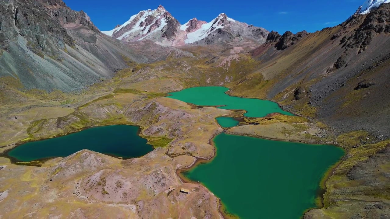 Una spettacolare ripresa aerea cinematografica con drone rivela le vibranti acque turchesi, ricche di minerali, delle Lagune Ausangate 7 ad alta quota, incastonate sotto imponenti cime andine innevate in Perù