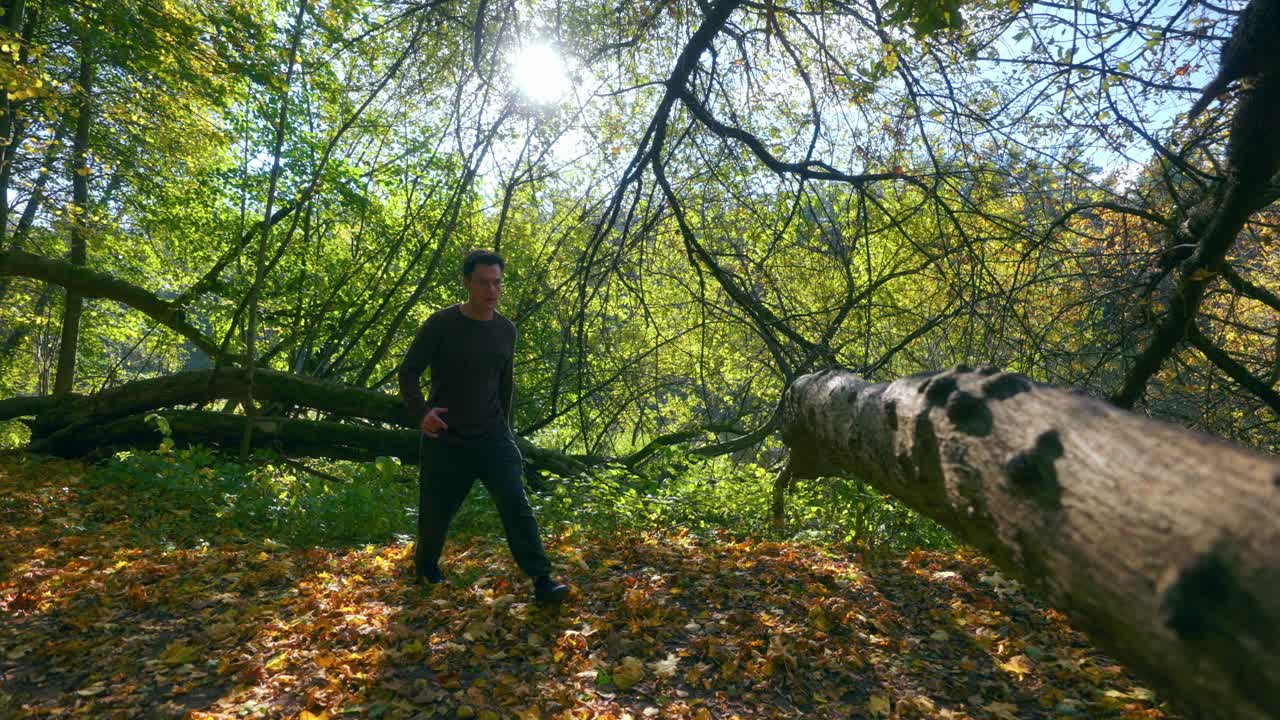 un joven activo saltando sobre el gran tronco de un árbol durante la temporada de otoño en lituania, europa - tiro de seguimiento