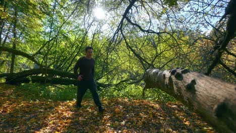 a young active man jumping over the big tree trunk during fall season in lithuania, europe- tracking shot