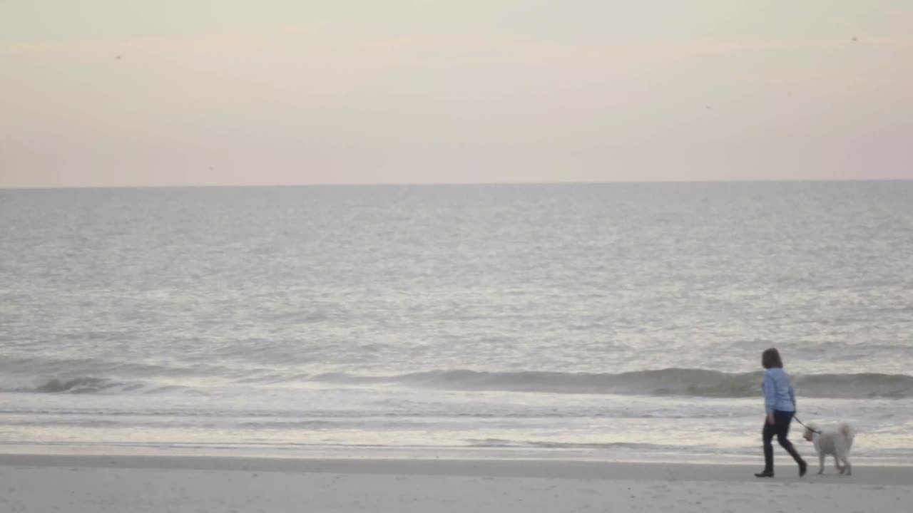 Woman walking across beach at sunrise.