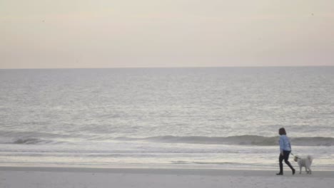 woman walking across beach at sunrise.