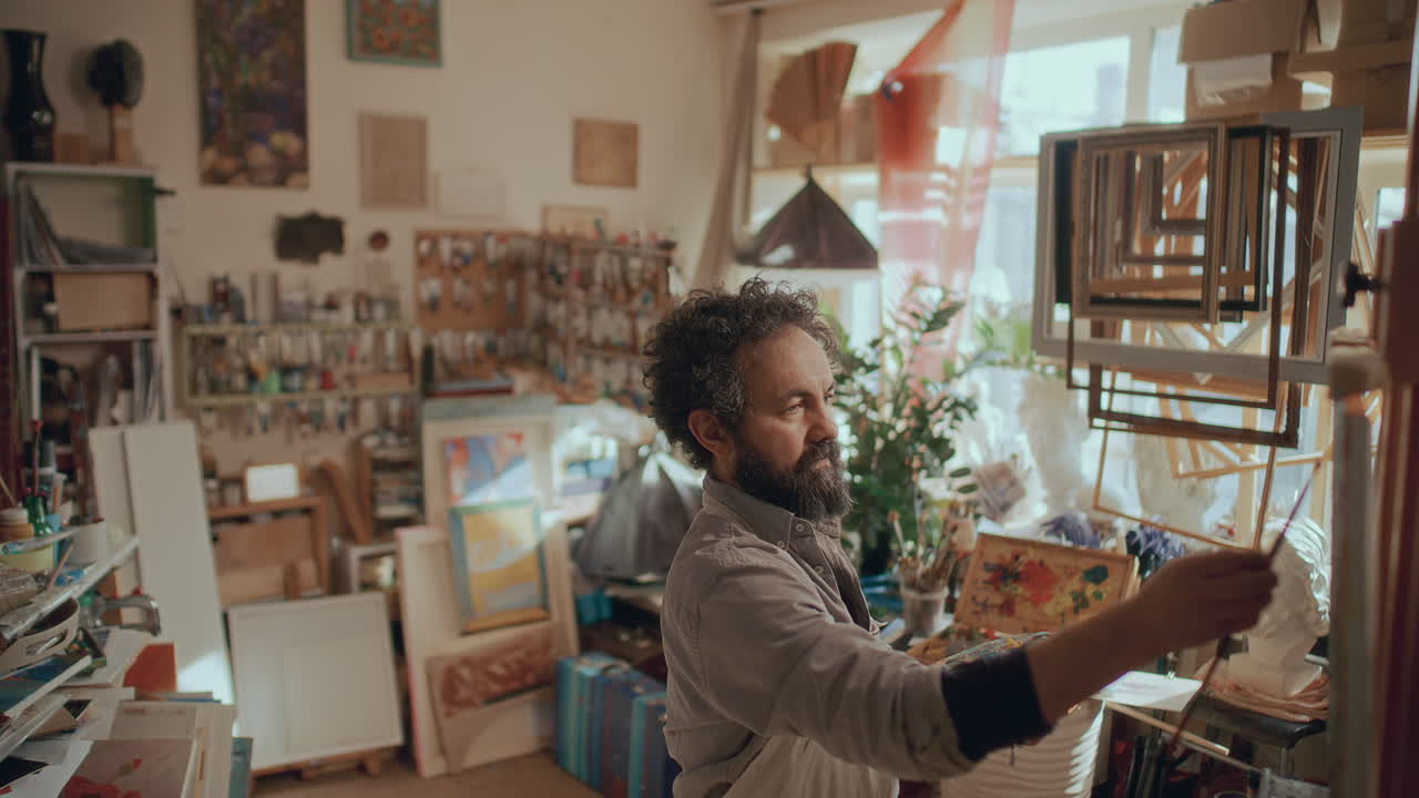 Maler arbeitet in einem sonnigen Atelier, umgeben von Künstlerbedarf.