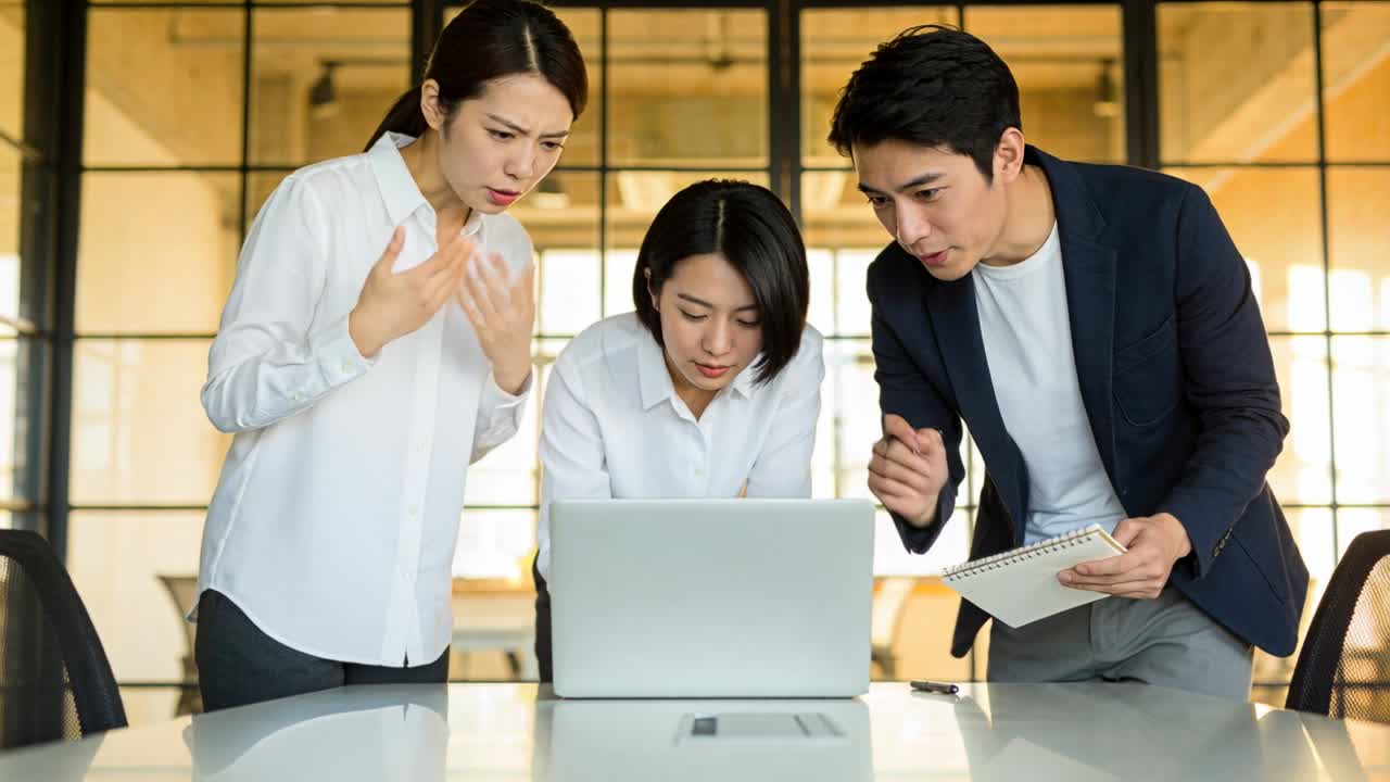 会議室のテーブルで話し合う3人の同僚。ラップトップとスパイラルノートを使用し、白いブラウスを着用している