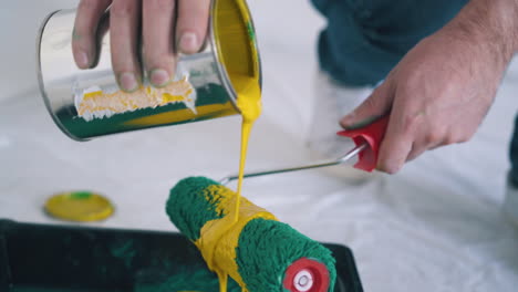 builder-pours-yellow-paint-onto-roller-above-tray-closeup