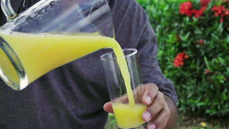 man serving in slow motion a nutritious orange juice from a jar to a glass outside in the morning camping in the nature