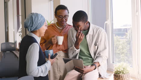 muslim businesswoman, businesswoman and young worker are laughing while looking something at tablet in the office 2