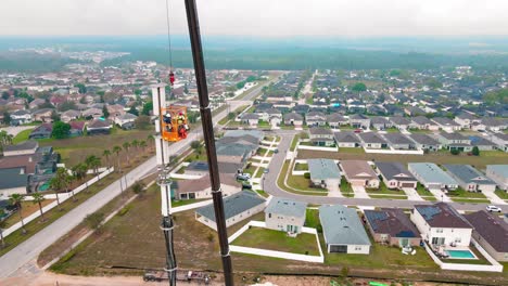 A-4k-aerial-shot-of-2-construction-workers-repairing-building-and-maintaining-a-radio-or-cell-tower-with-residential-houses-down-below-them-in-Florida