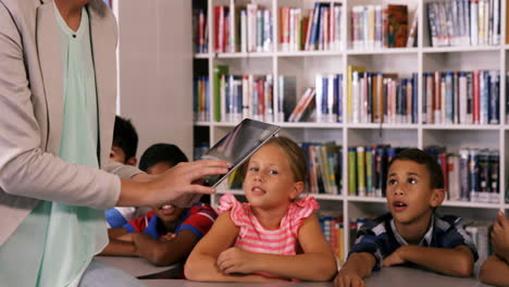 Teacher-teaching-school-kids-on-digital-tablet-in-library