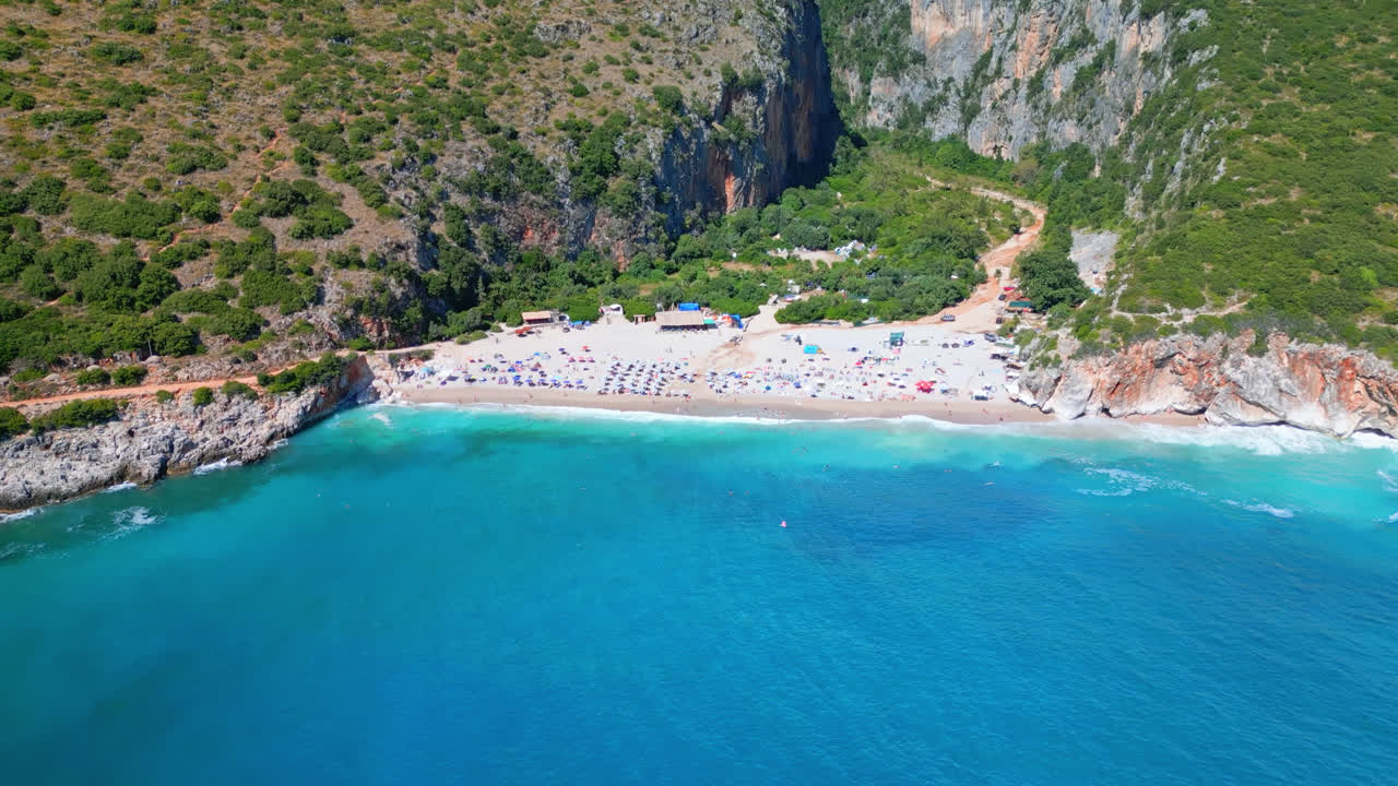 Aerial drone backward moving shot over turquoise sea water of the Ionian sea with sandy beach and impressive canyon through mountains in background