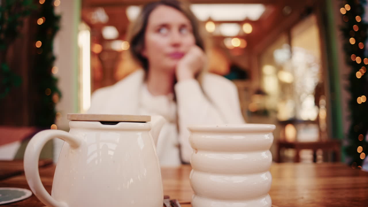 くつろげるカフェの木のテーブルに座って、再利用可能な折りたたみ式カップを持つ女性