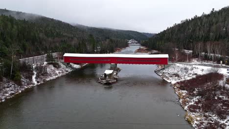 covered bridge with a little bit of snow crossing a river in quebec, canada