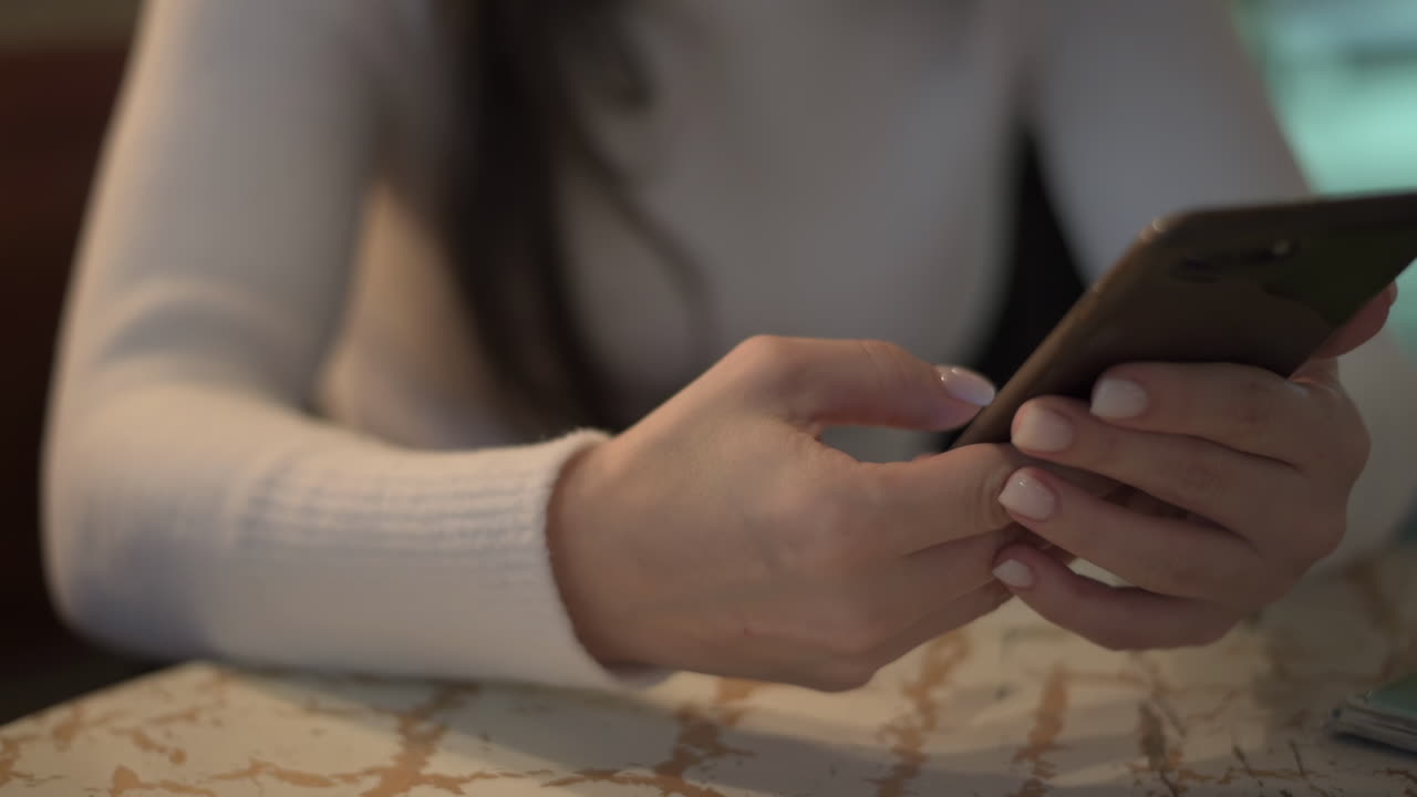 Close up of a woman scrolling on her phone at a table at a cafe
