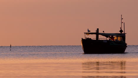 fishing boat rests calmly at sea during golden sunrise, seagull perched on roof