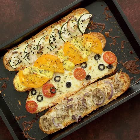 long baguettes pizza sandwiches with tuna  mushrooms  tomatoes and cheese on a metal baking tray