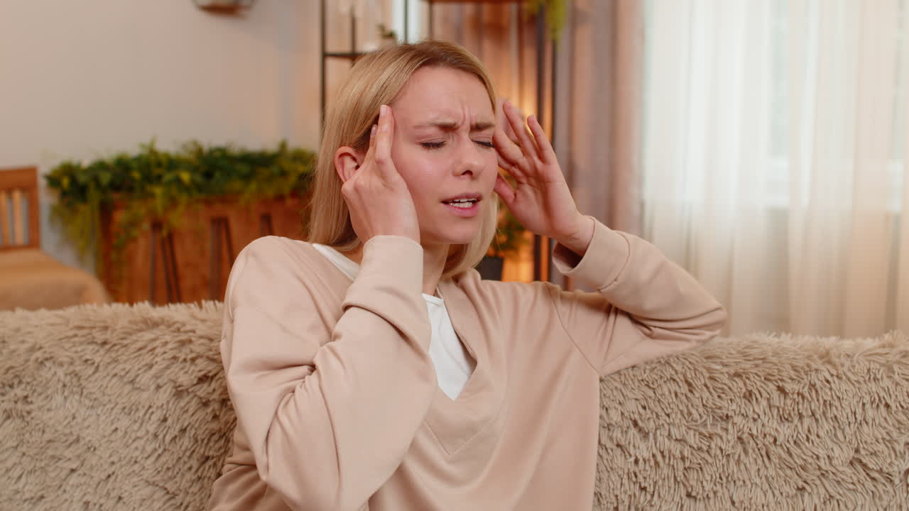 Adult woman holding head with both hands at home experiencing migraine stress high blood pressure
