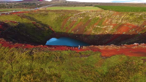 aerial revealing shot of tourists walking around the kerid crater and lake in iceland