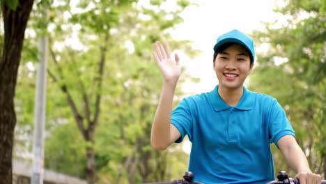 a cheerful delivery worker in a blue uniform rides through a vibrant park. they wave to passersby, enjoying a pleasant day outdoors amidst lush greenery.