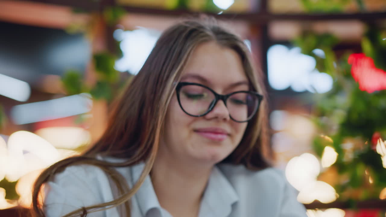 primer plano de una dama elegante con gafas, sonriendo mientras se centra en el teléfono operativo, las cálidas luces bokeh en el fondo mejoran la atmósfera interior moderna y elegante