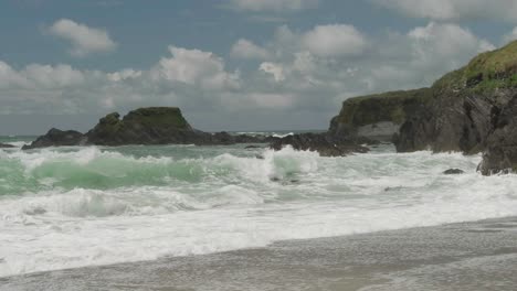 Cliffs-and-crashing-waves-on-the-beach-with-white-clouds-passing-on-a-blue-sky-in-slow-motion