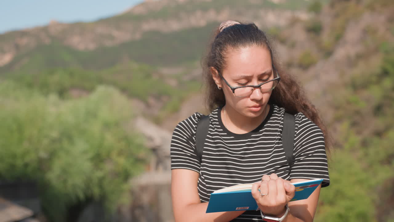 Viaggiatrice creativa che scrive un diario vicino a rovine fluviali con penna e taccuino, espressione pensierosa e passo calmo, sfondo architettonico e luce solare soffusa, creazione di contenuti spontanea e umore riflessivo.