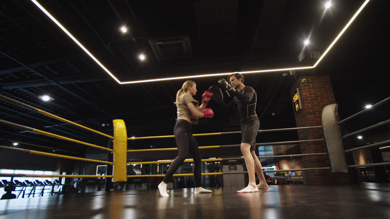 Donna sportiva rigorosa che si allena sulla tecnica in palestra. Ragazza in forma che si allena con l'allenatore.