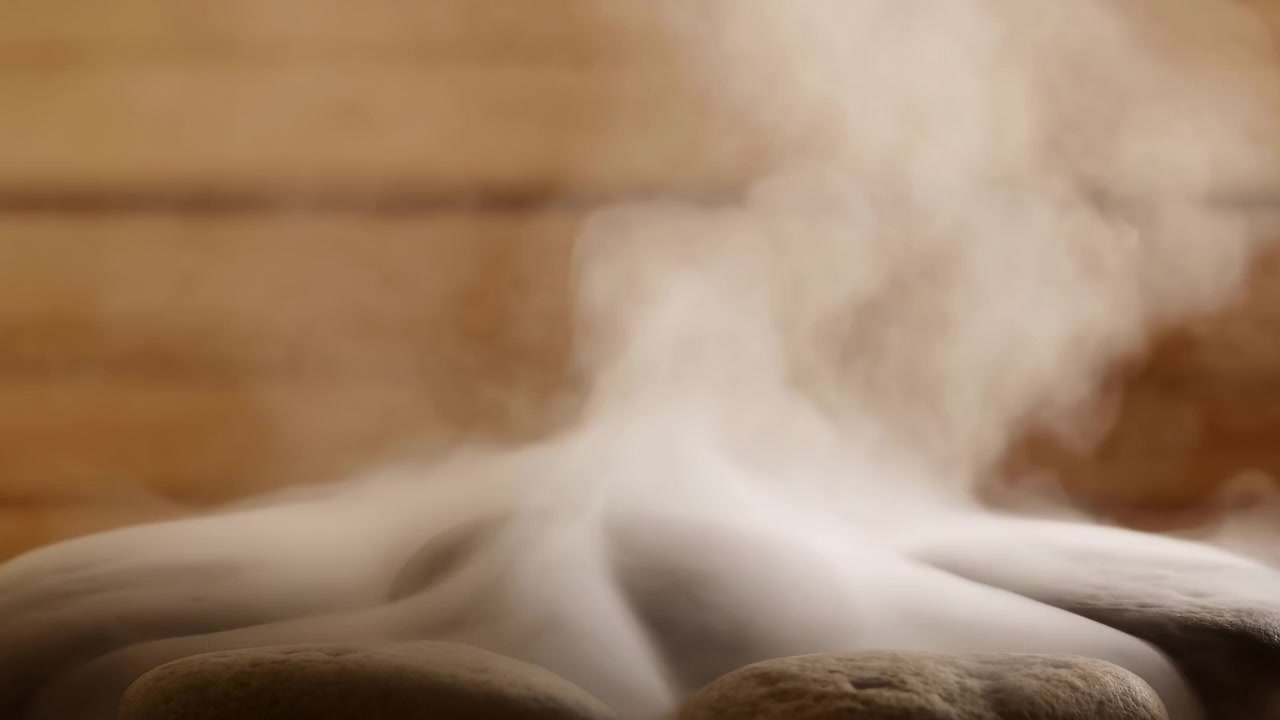 Dense warm steam rises and billows above smooth rounded spa stones, forming shifting plumes and vapor layers that softly obscure stone tops inside indoor wooden wellness setting with gentle diffuse